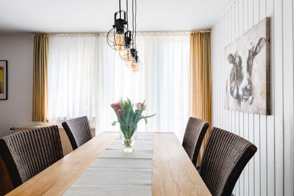 Esszimmer mit langer Tischplatte, Stühlen und Blumenarrangement.