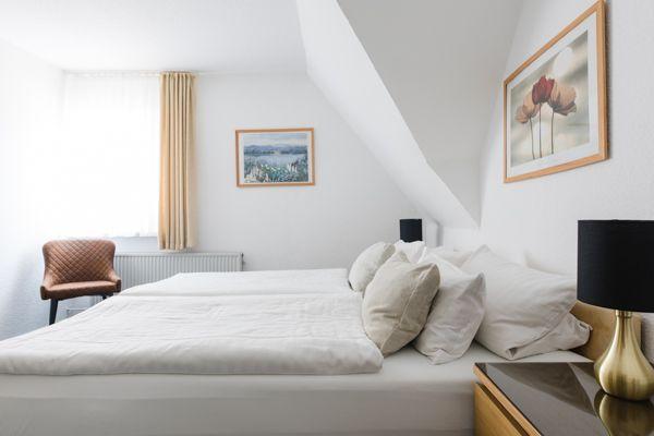 Schlafzimmer mit Doppelbett, Stuhl und Wandbildern unter schräger Decke.