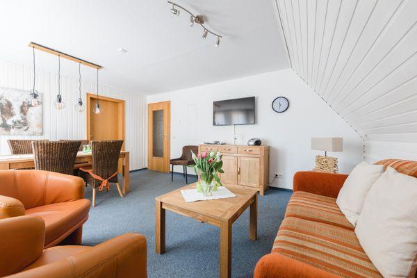 Wohnbereich mit Sofa, Sessel und Esstisch unter schrägem Dach