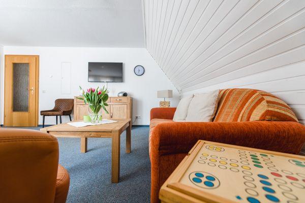 Wohnzimmer mit Sofa, Tisch und Fernseher unter schräger Decke.