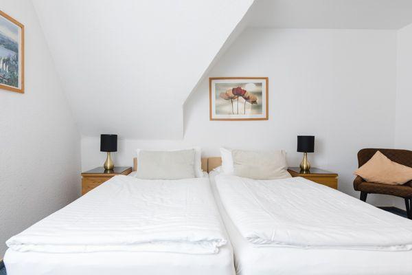 Zwei Betten mit weißen Bettwäsche, Nachttische und Bilder an der Wand.