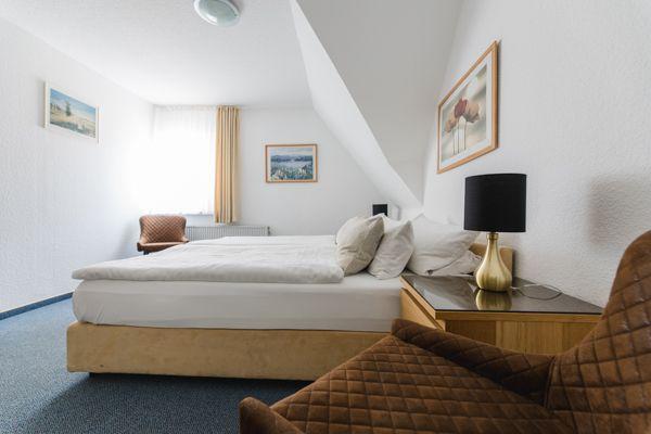 Schlafzimmer mit Dachschräge, Bett, Nachttisch und Sessel.