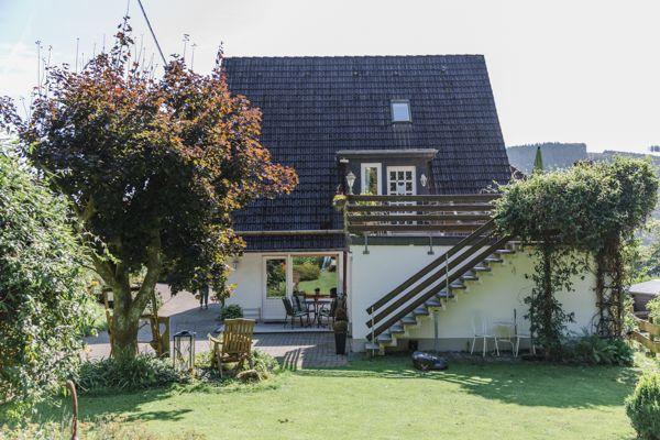 Haus mit Terrasse, Garten und Holztreppe zur oberen Etage.