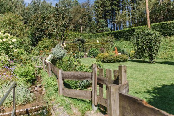 Garten mit Holzgeländer, Blumenbeeten und grünem Rasenhang