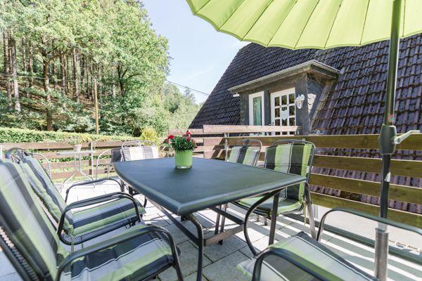 Terrasse mit Tisch, Stühlen und grünem Sonnenschirm vor einem Haus.
