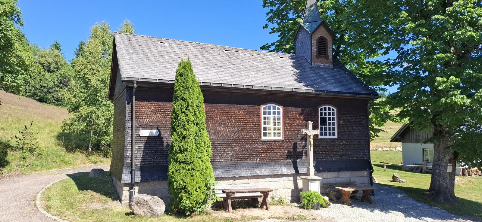 Wooden church with cross and benches in greenery
