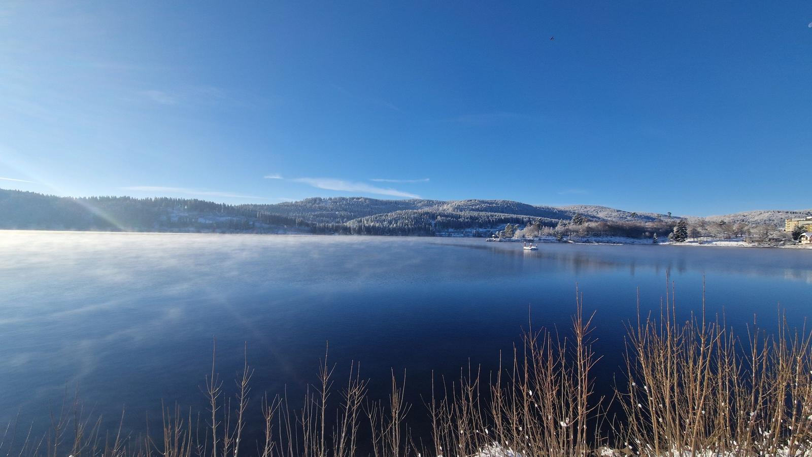 Snow-covered hills surround a calm lake with a small boat.