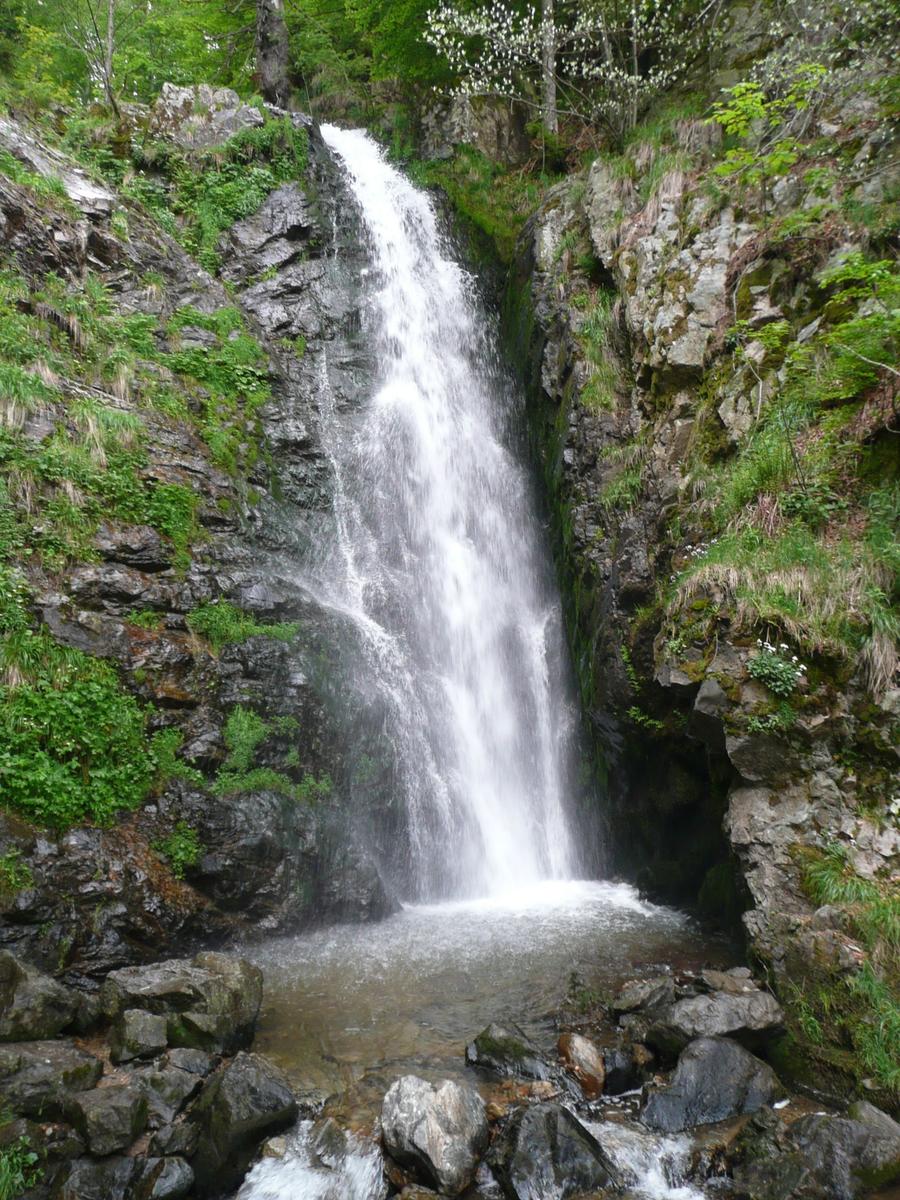 Waterfall flows into a stream, surrounded by rocks and greenery.