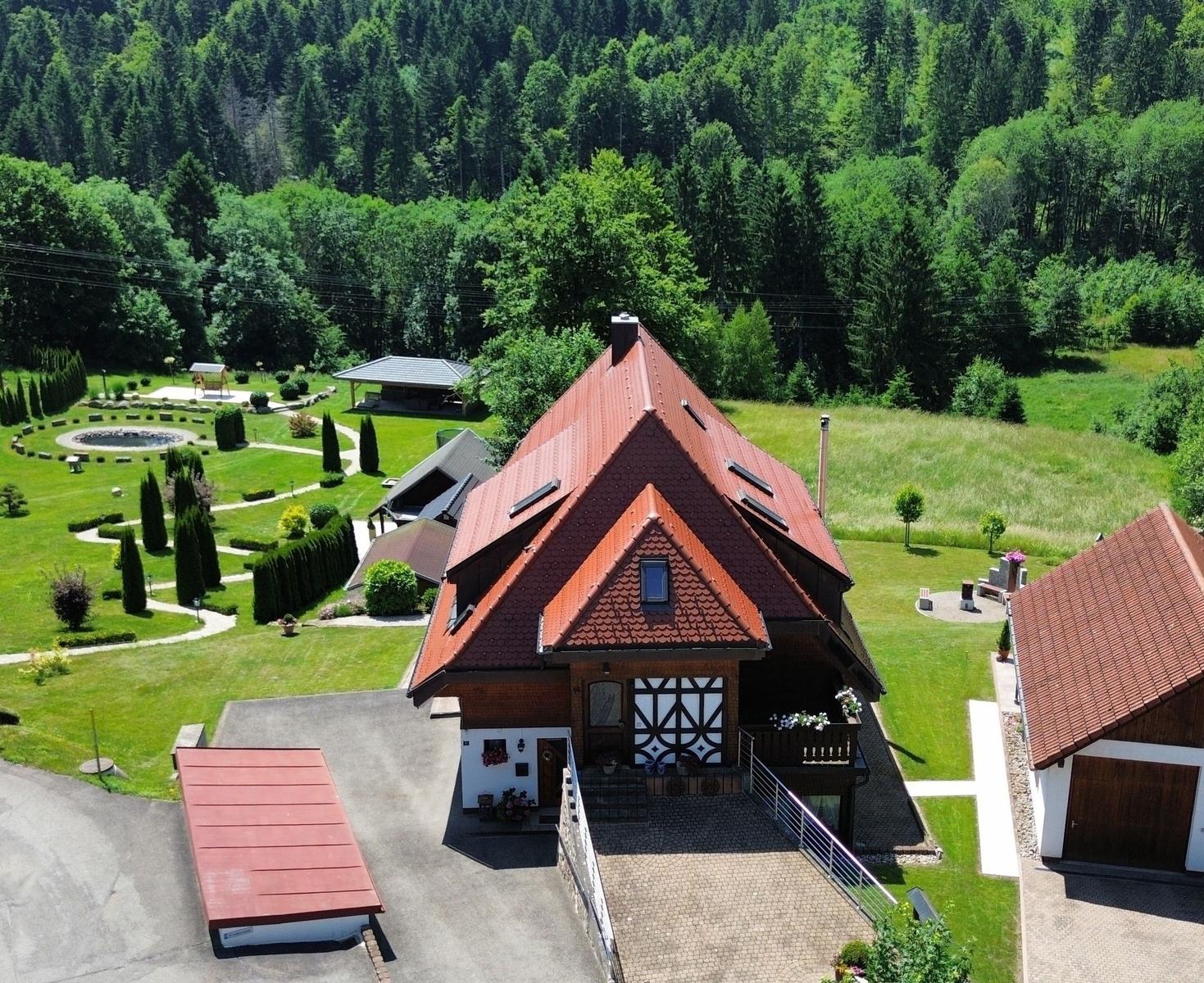 House with red roof, large garden, and forest in the background.