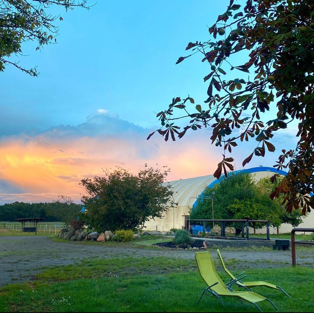 Zwei grüne Liegestühle vor einem Bauernhof bei Sonnenuntergang.