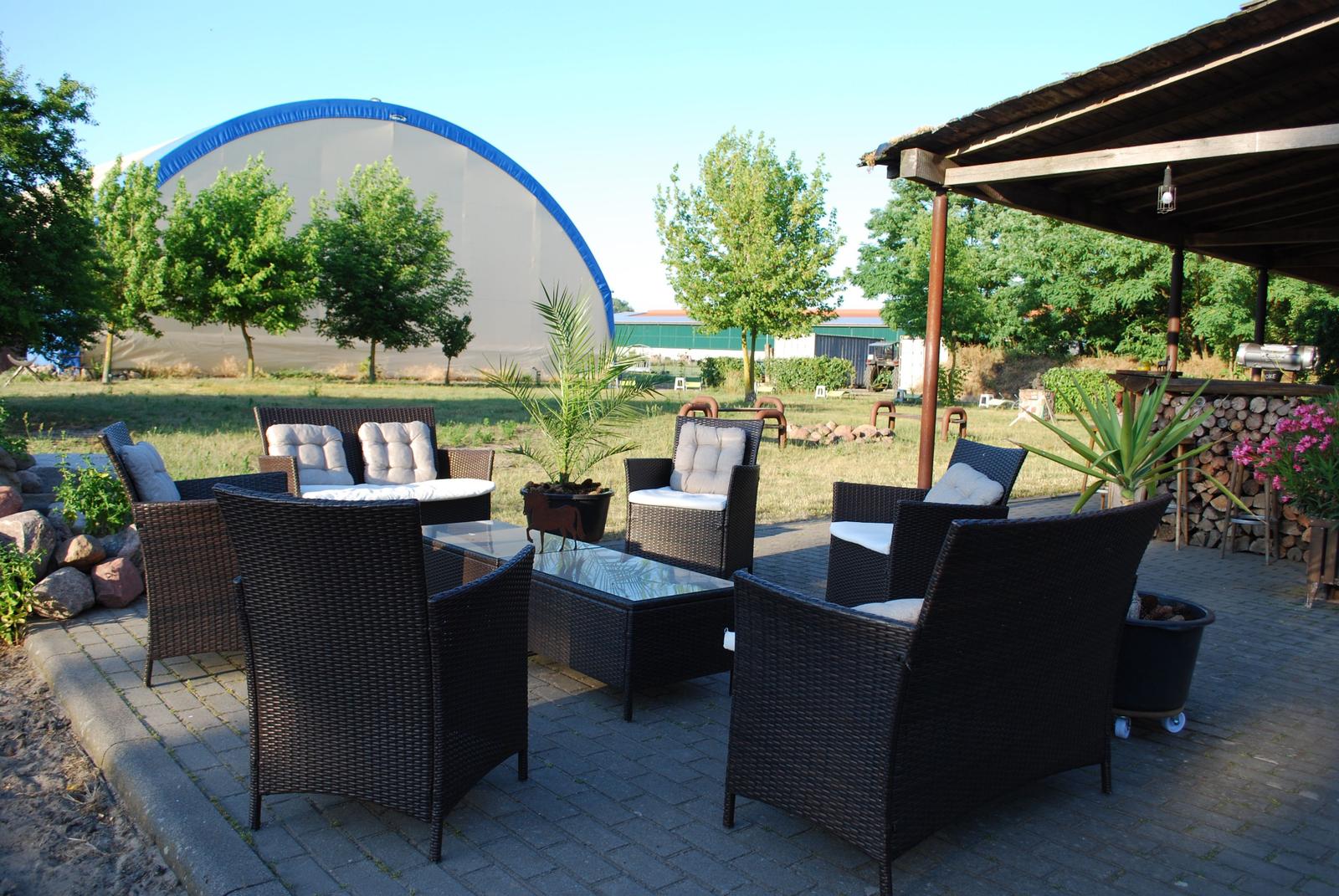 Terrasse mit Sitzgruppe, Grill und Holzstapel im Hintergrund.