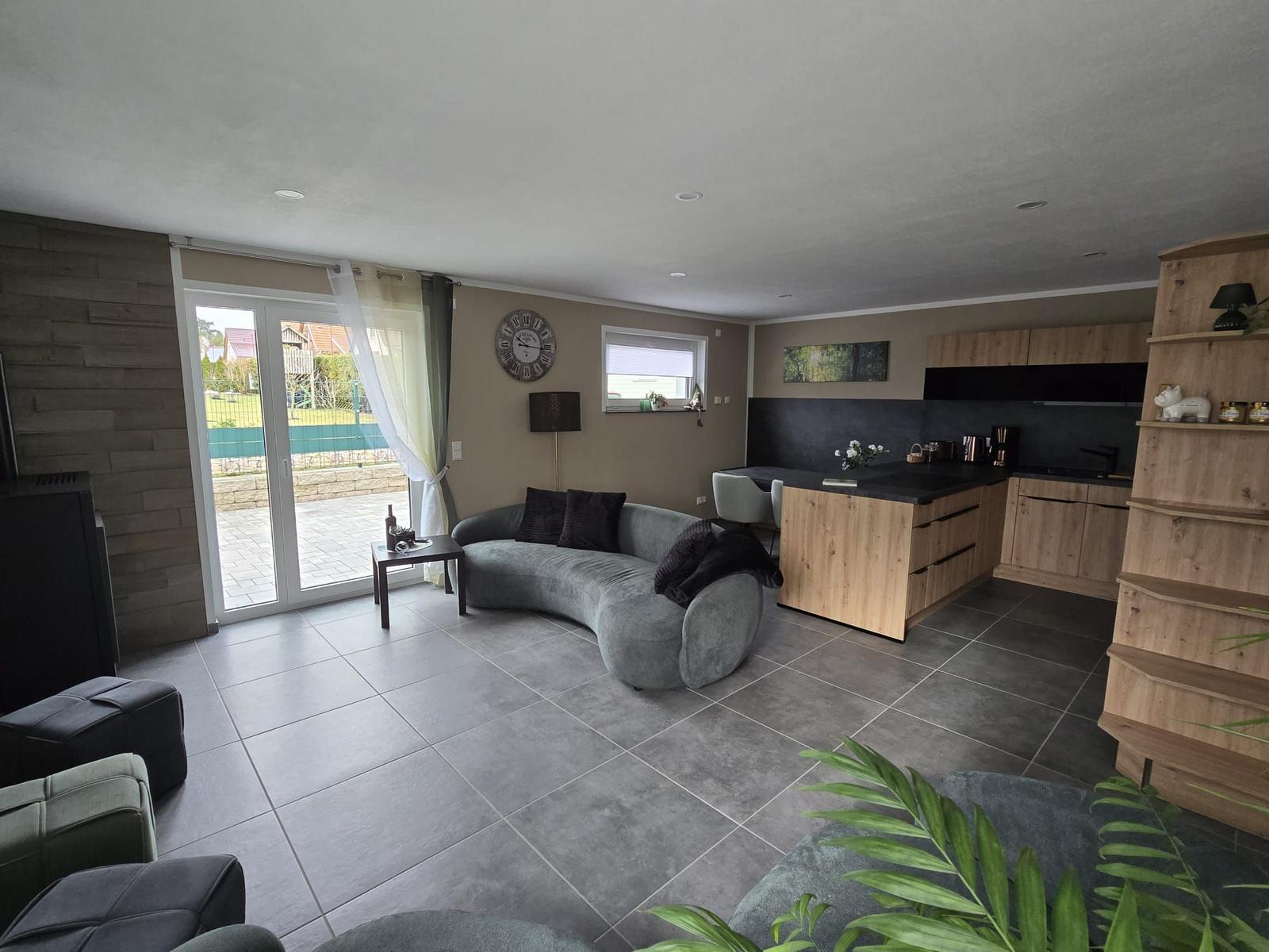 Wohn- und Küchenbereich mit Sofa, Kücheninsel und Terrassentür.