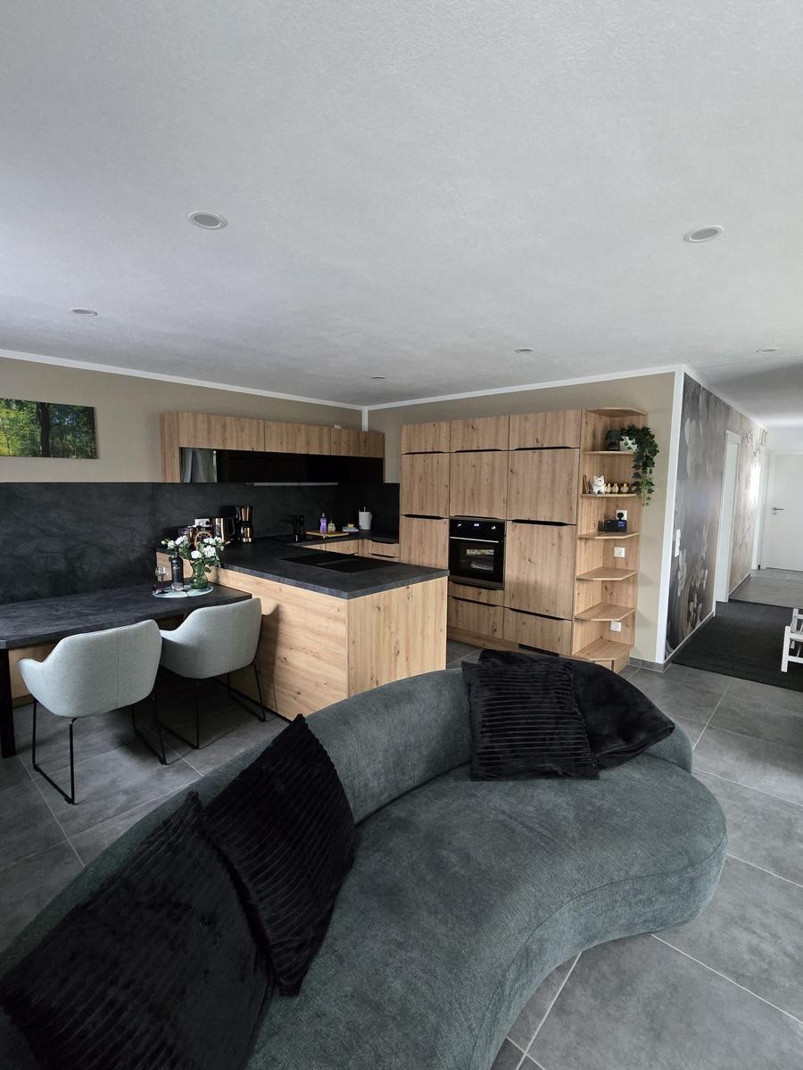 Wohnküche mit Holzmöbeln, grauem Sofa und Küchentisch mit Stühlen.