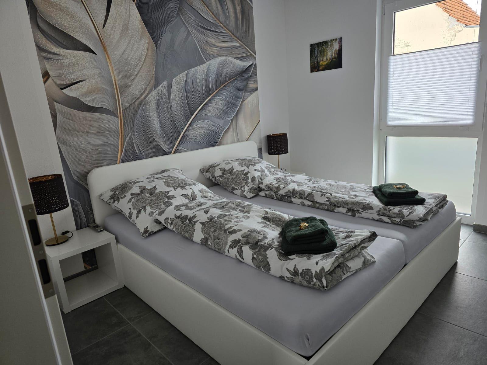 Schlafzimmer mit Doppelbett, floraler Bettwäsche und großen Fenstern.