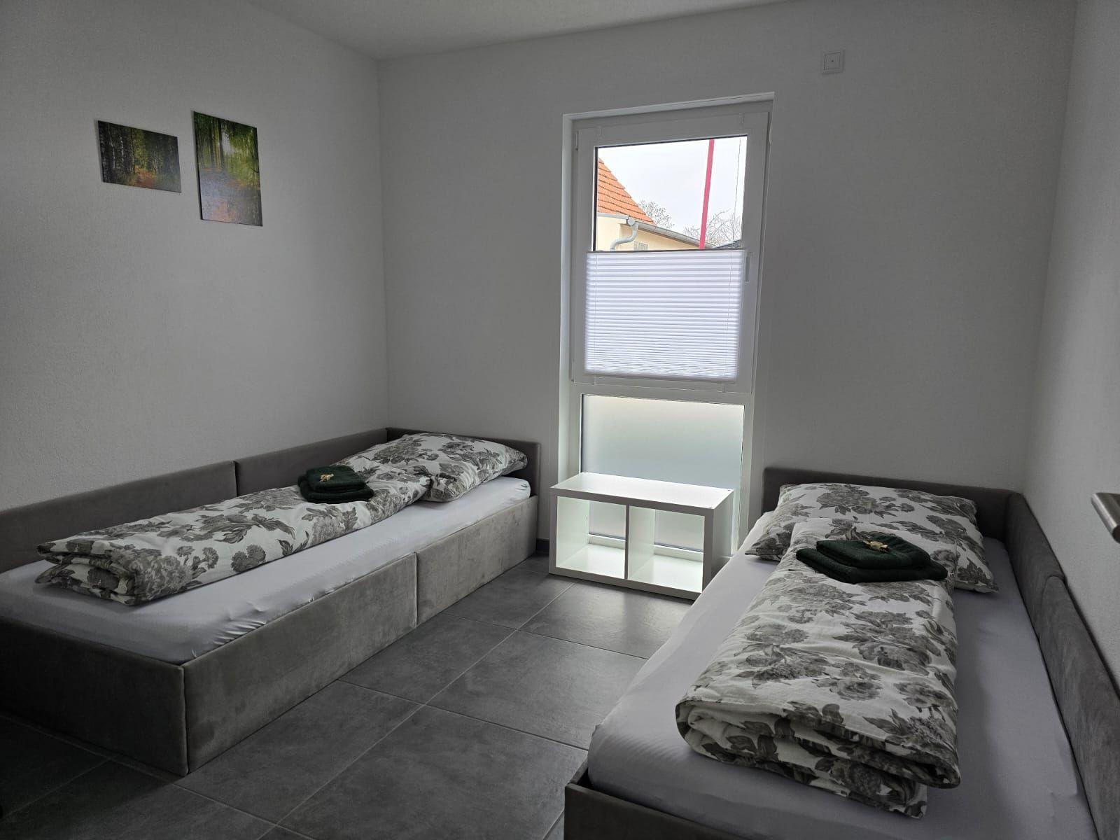 Zwei Einzelbetten mit floraler Bettwäsche und Fenster mit Jalousie.