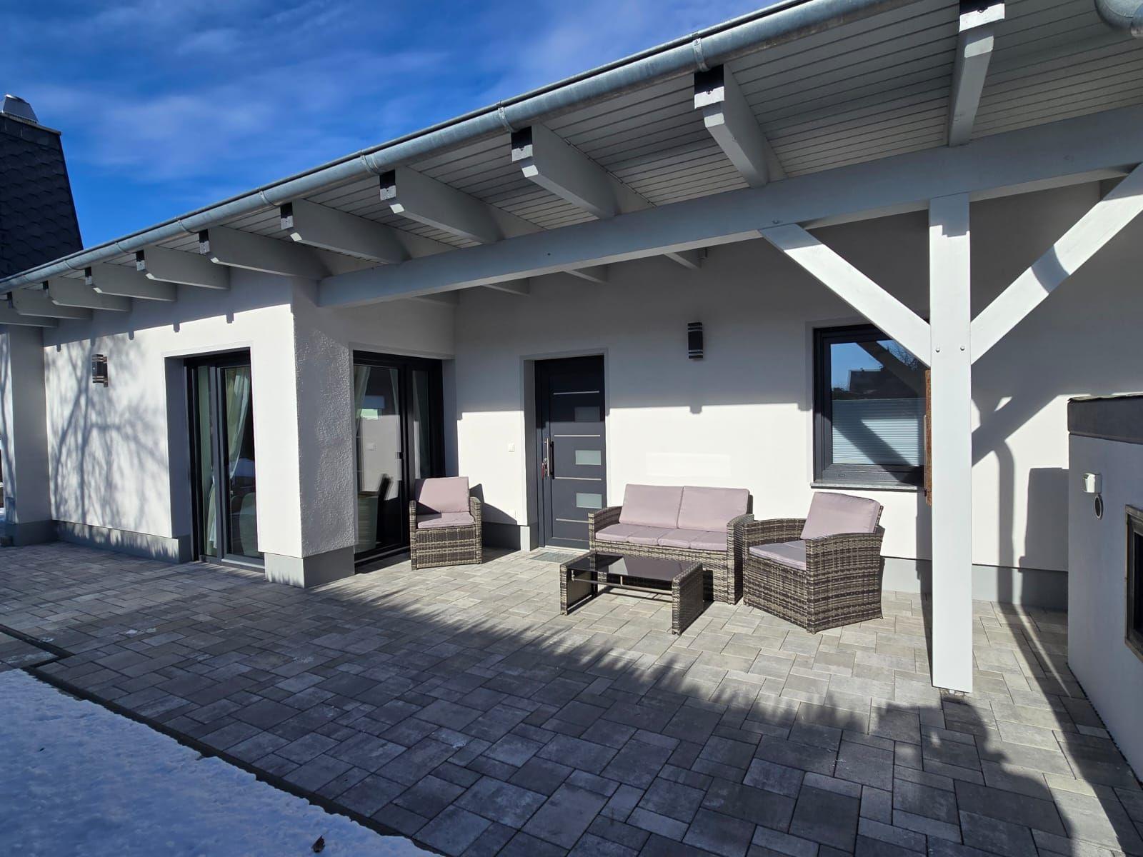 Terrasse mit Sitzgruppe unter Dach, glasierte Fliesen und Eingangstür.