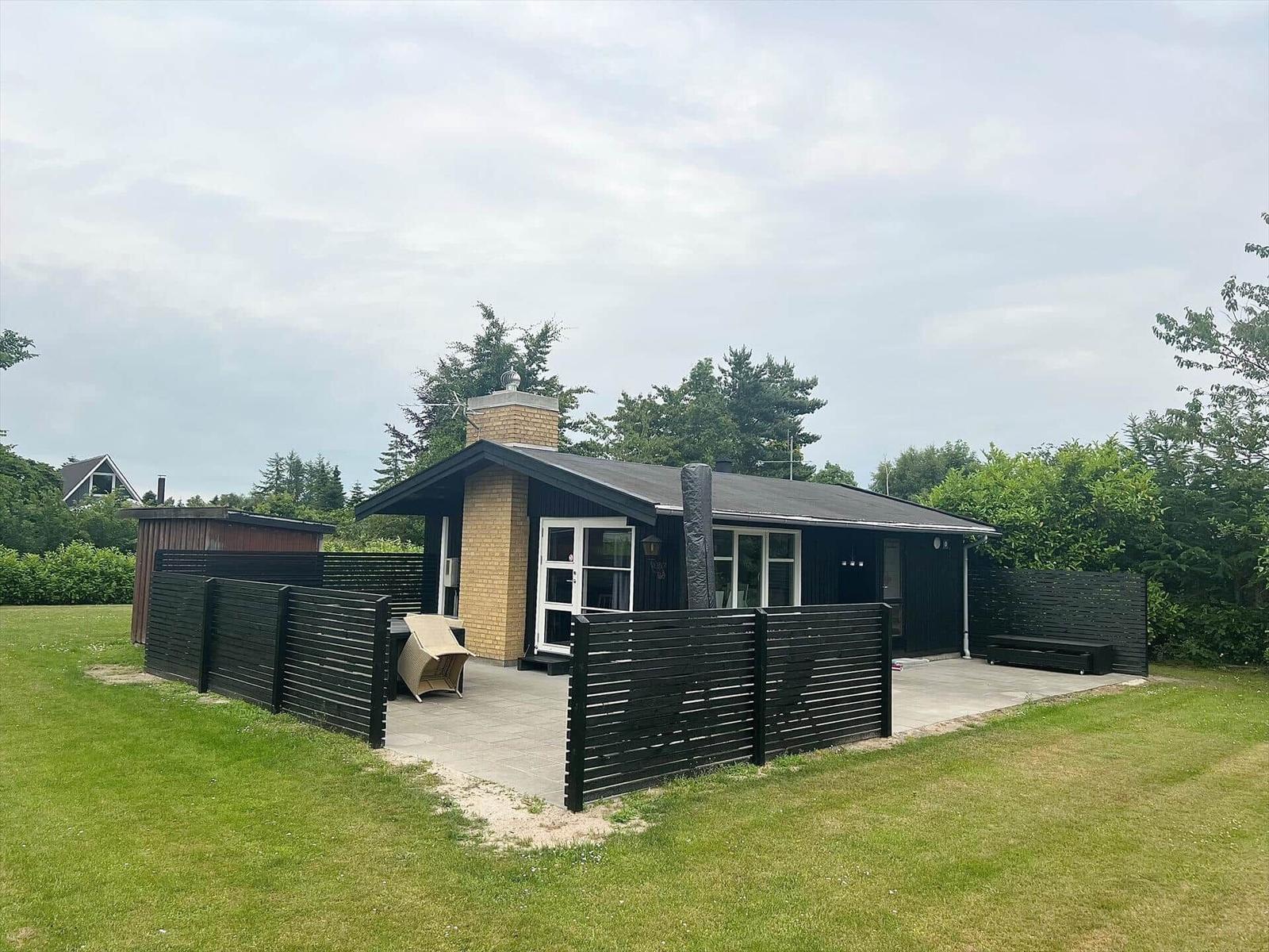 Modern villa with terrace, garden, and wooden fence. Entrance door and windows are visible.