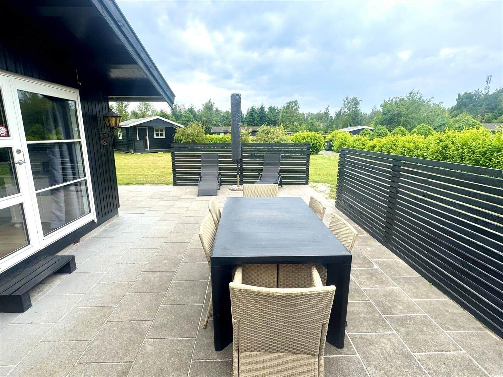 Terrace with table, chairs, and loungers. Black wooden fences and green garden.