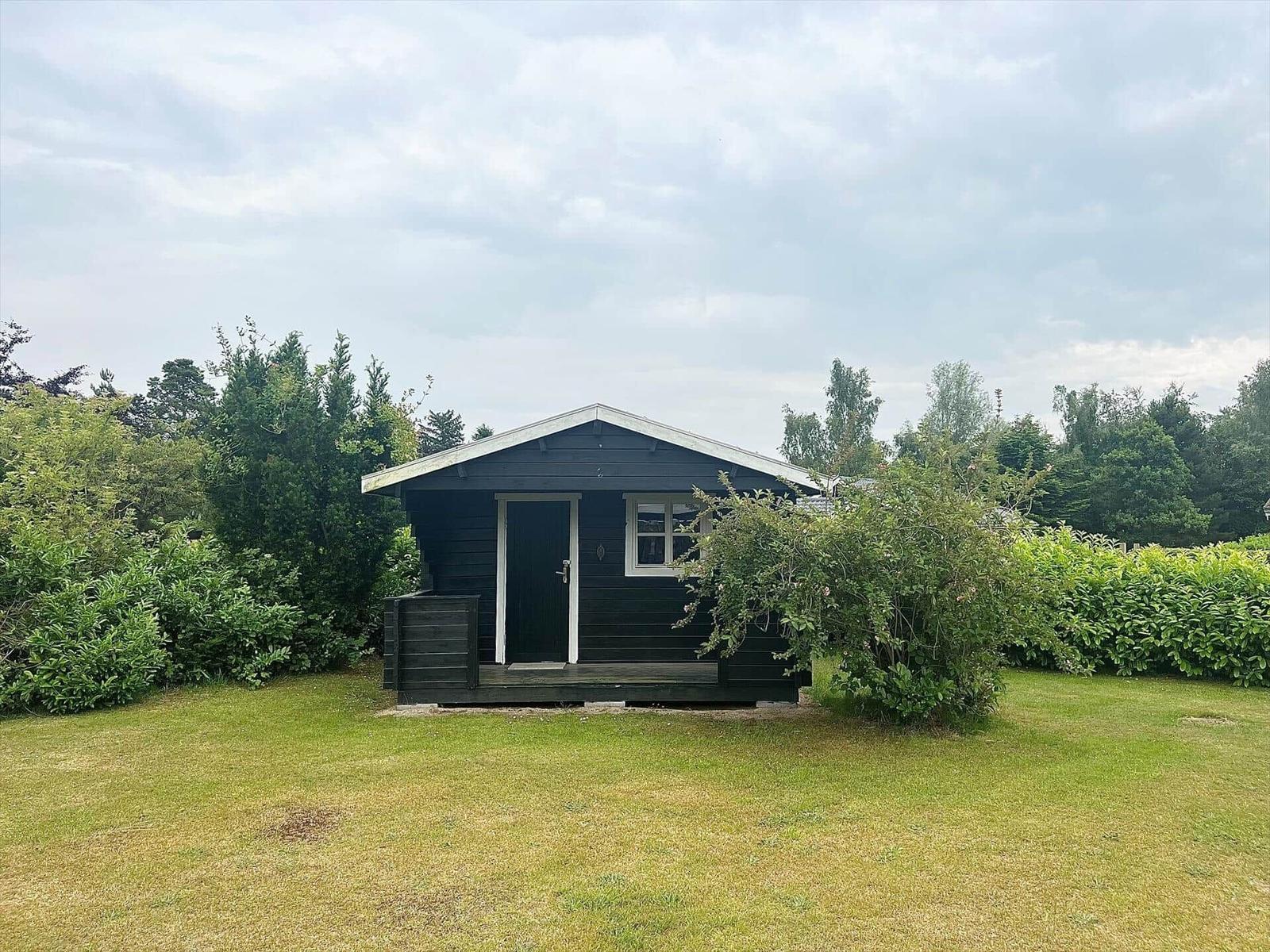Black wooden house with white window frames and door, surrounded by grass and shrubs.