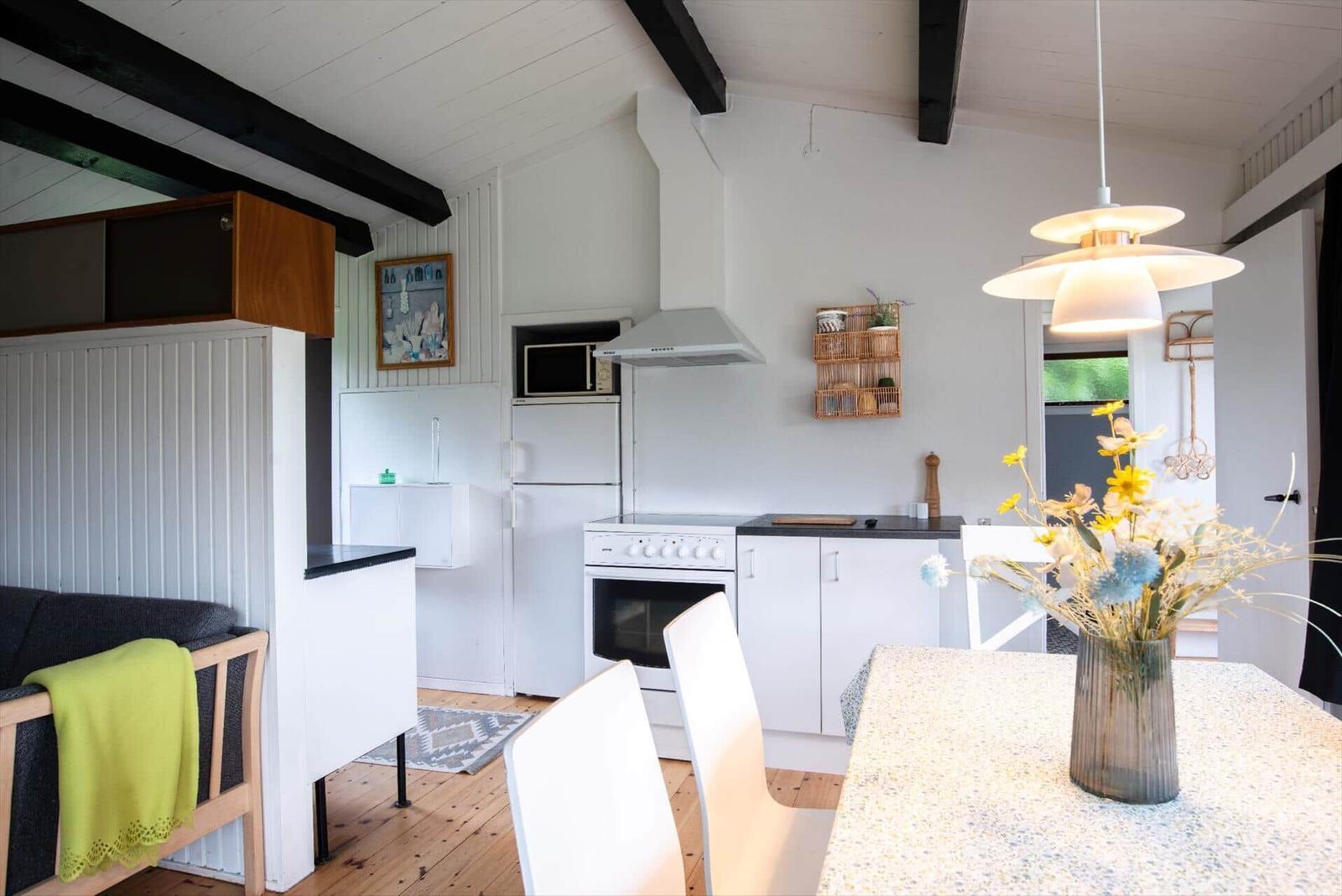 Kitchen with white built-in cabinetry, dining table, and seating. Wooden floor and black beams.