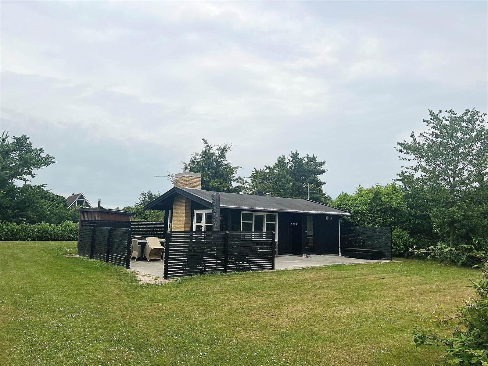 A simple house with garden and terrace, surrounded by trees.