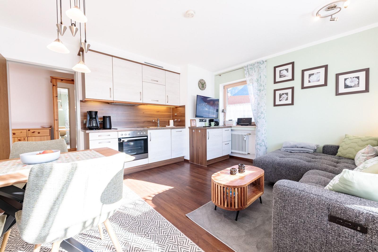 Wohnküche mit Essbereich, Sofa und Fernseher. Holzboden und hell gestrichene Wände.