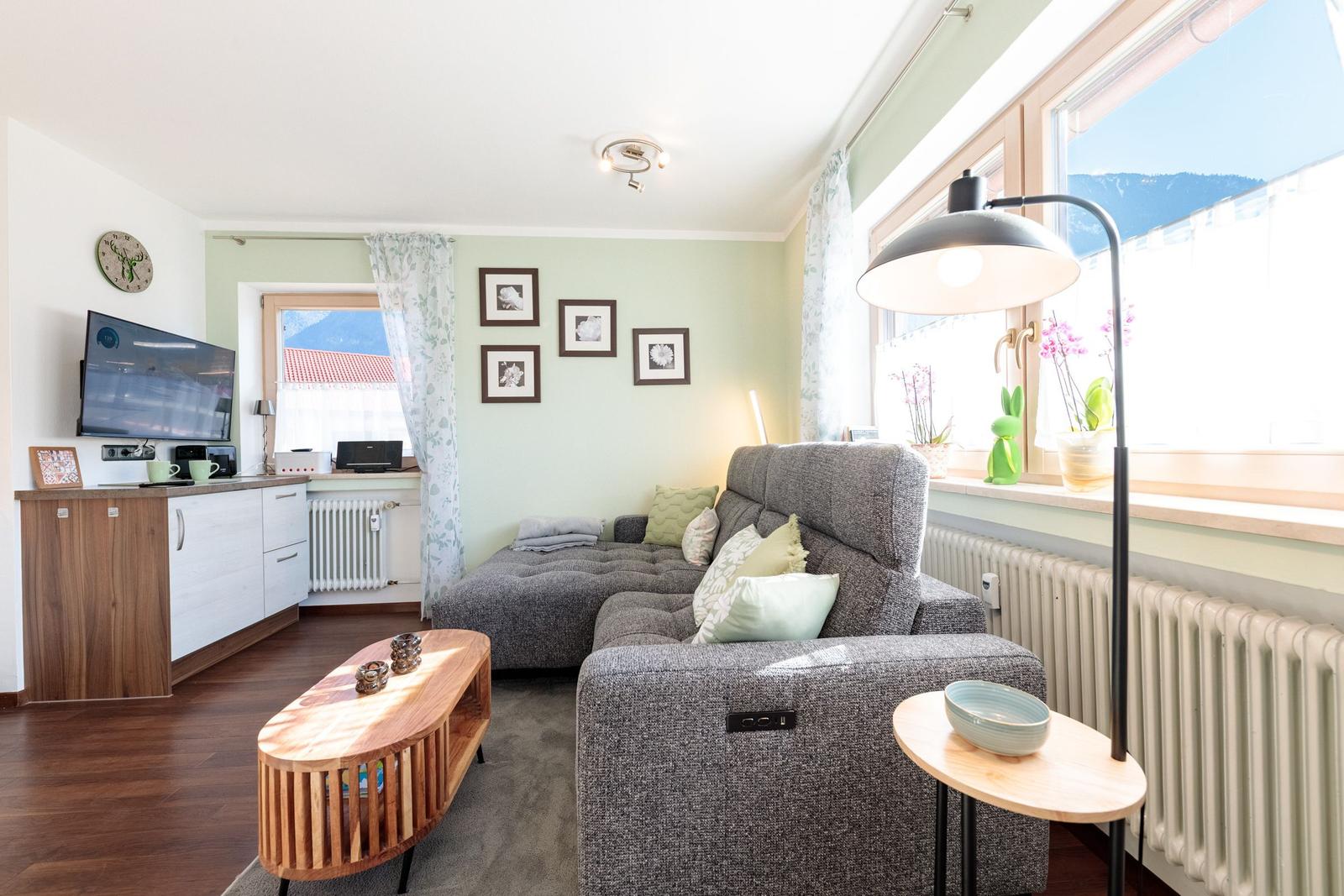 Wohnzimmer mit Sofa, Couchtisch und Fernseher. Fenster mit Blick auf Berge.