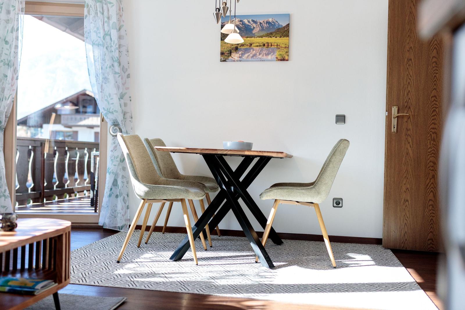 Esstisch mit vier Stühlen vor einem Fenster mit Blick auf Balkon.