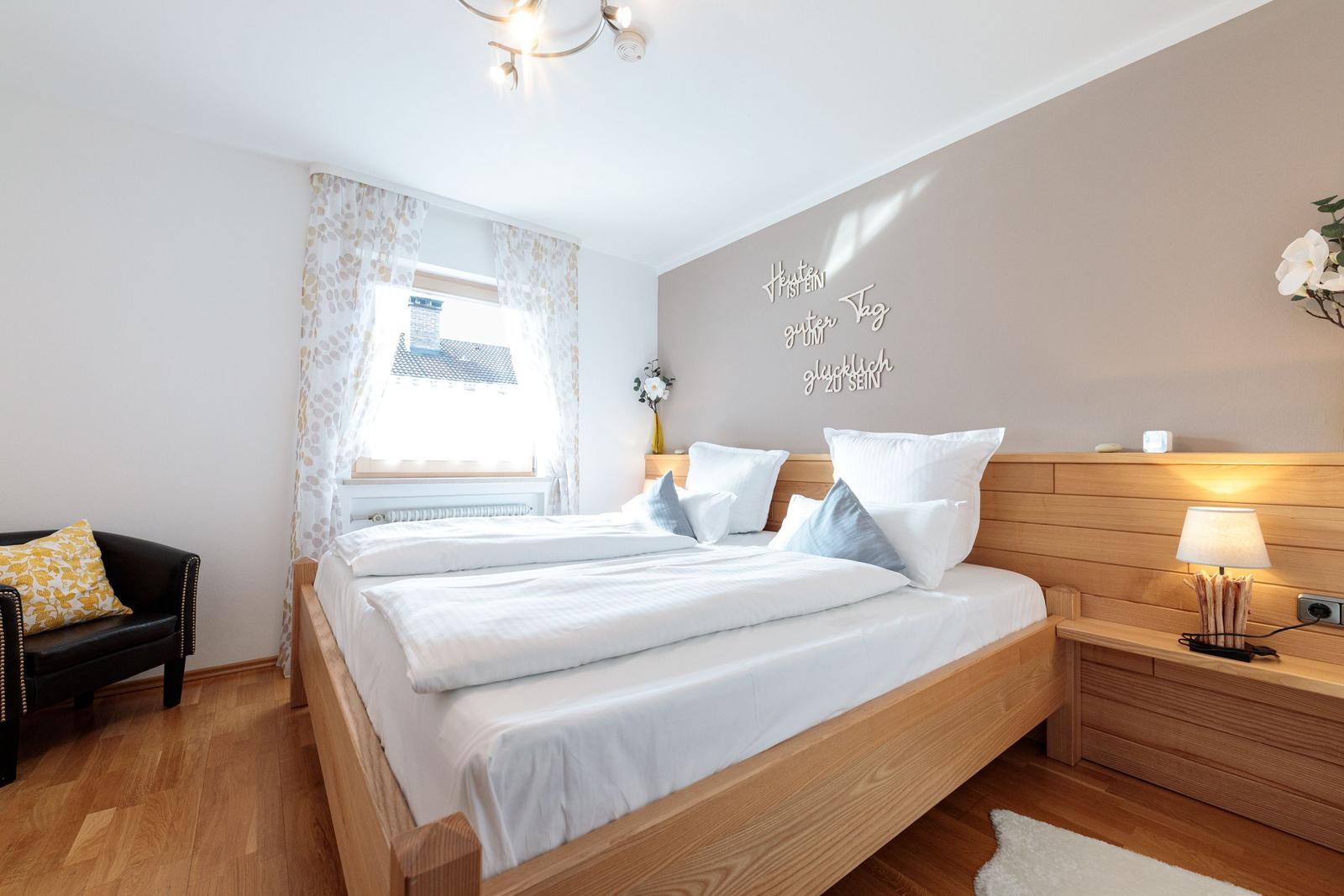 Schlafzimmer mit Holzbett, Fenster und Nachttisch.