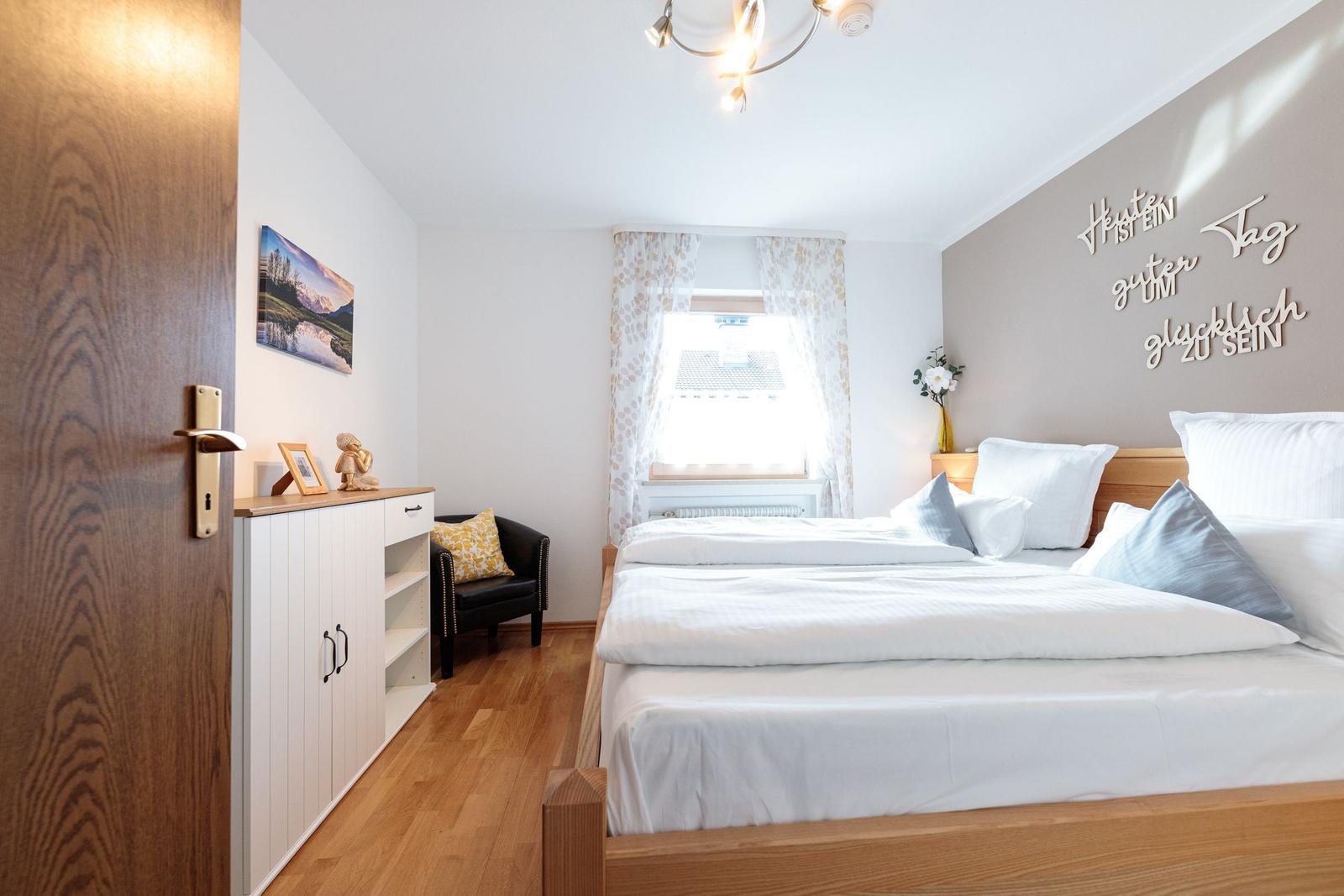 Schlafzimmer mit Bett, Schrank und Fenster mit Vorhängen.