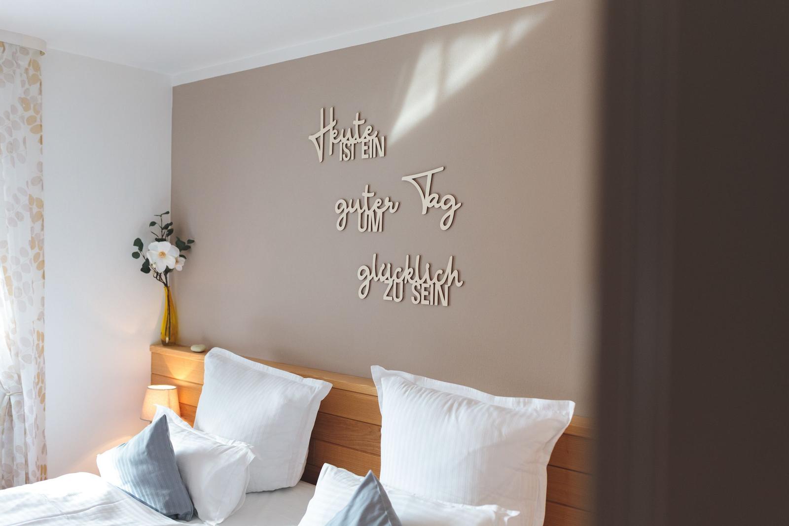 Schlafzimmer mit Bett, Wanddekoration und Blumenvase.