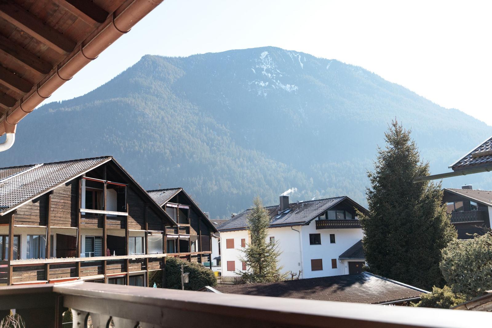 Blick auf Berge mit Wald, traditionelle Häuser und Balkon im Vordergrund.
