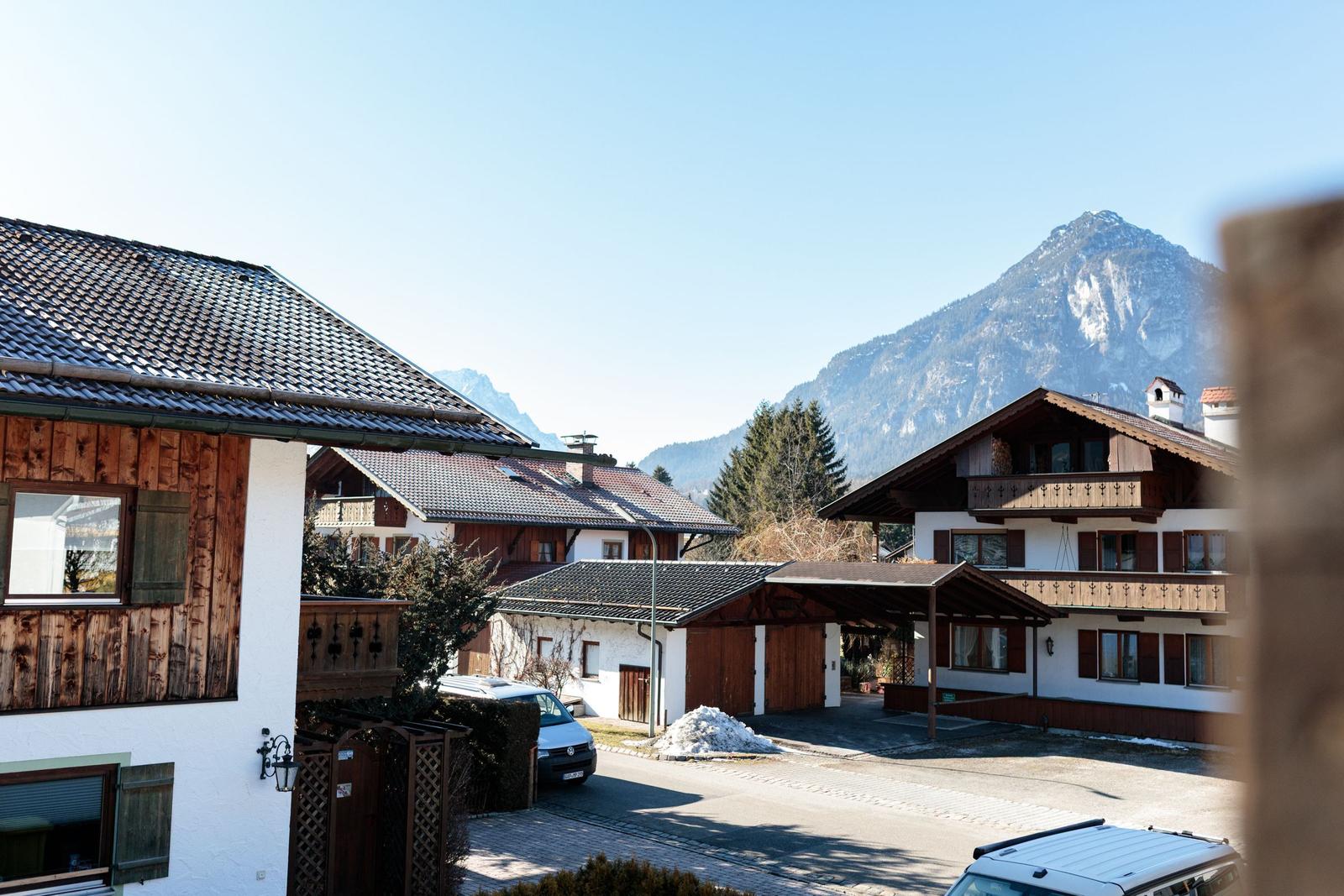 Haus mit Balkon und Bergblick. Parkplatz und Schneehaufen sichtbar.