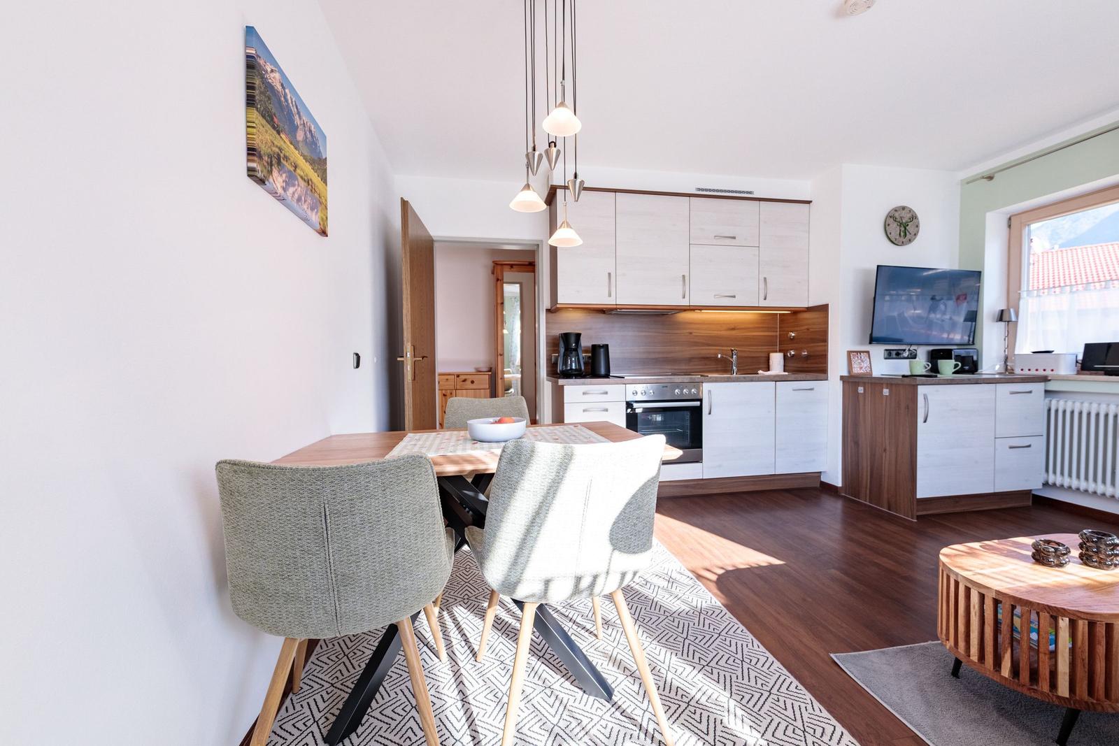 Essbereich mit Tisch, Stühlen und Küchenbereich im Hintergrund.