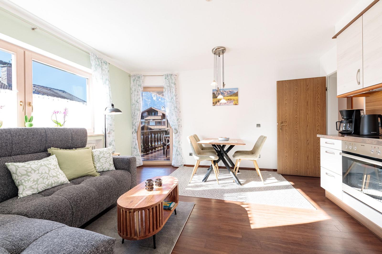 Wohn- und Essbereich mit Sofa, Tisch, Küchenzeile und Balkontür.