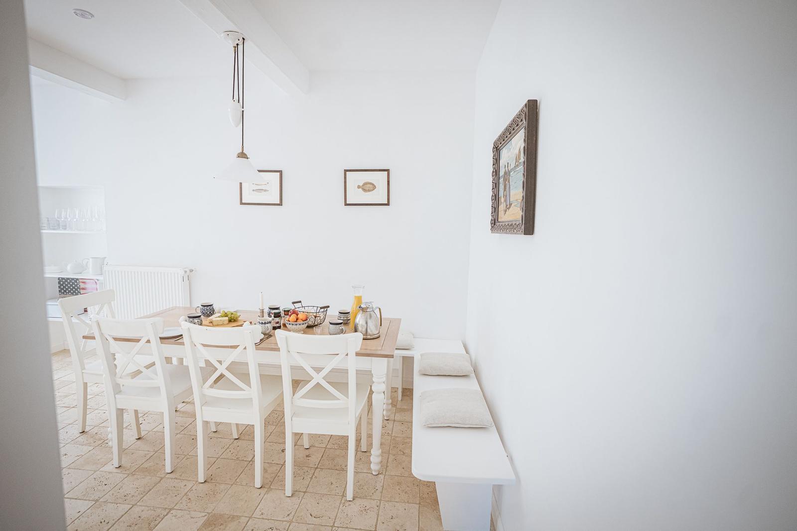 Esszimmer mit weißem Tisch und Stühlen, Wandbildern und Bänkchen mit Kissen.