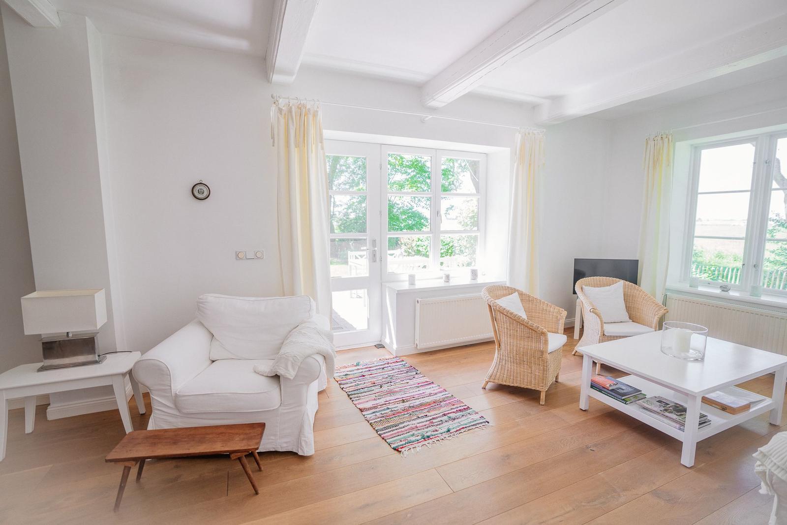 Wohnzimmer mit weißem Sofa, Rattanstühlen und Holzboden. Fenster mit Blick auf Garten.