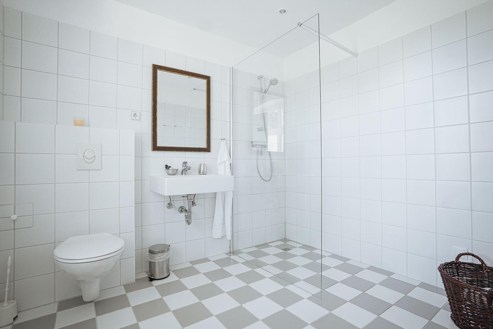 Badezimmer mit Dusche, Waschbecken und Toilette. Fliesenboden mit Schachbrettmuster.