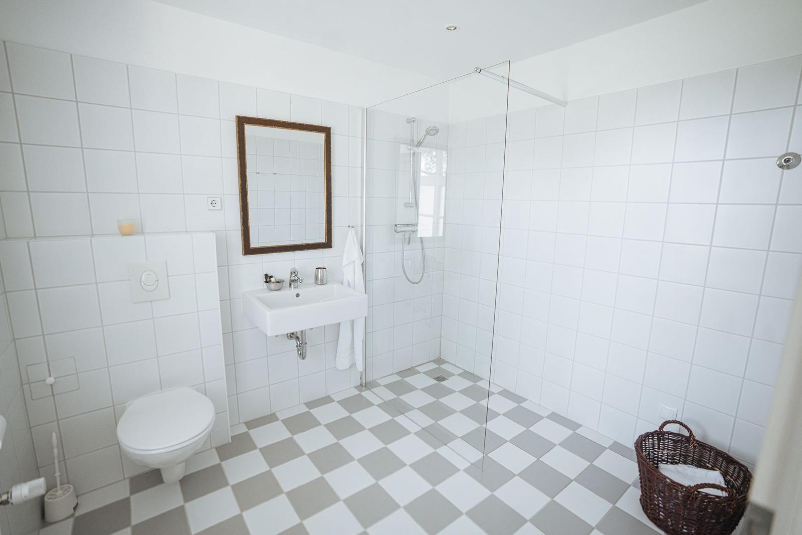 Badezimmer mit Dusche, Waschbecken und Toilette. Fliesenboden und Spiegel.