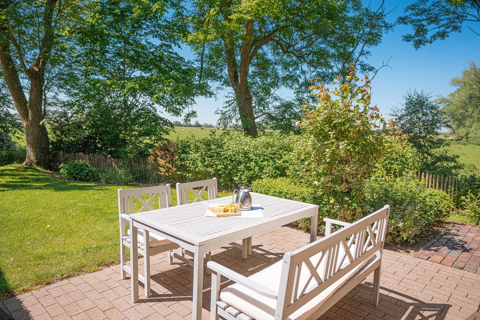 Terrasse mit Tisch und Bänken, umgeben von Grün und Bäumen.