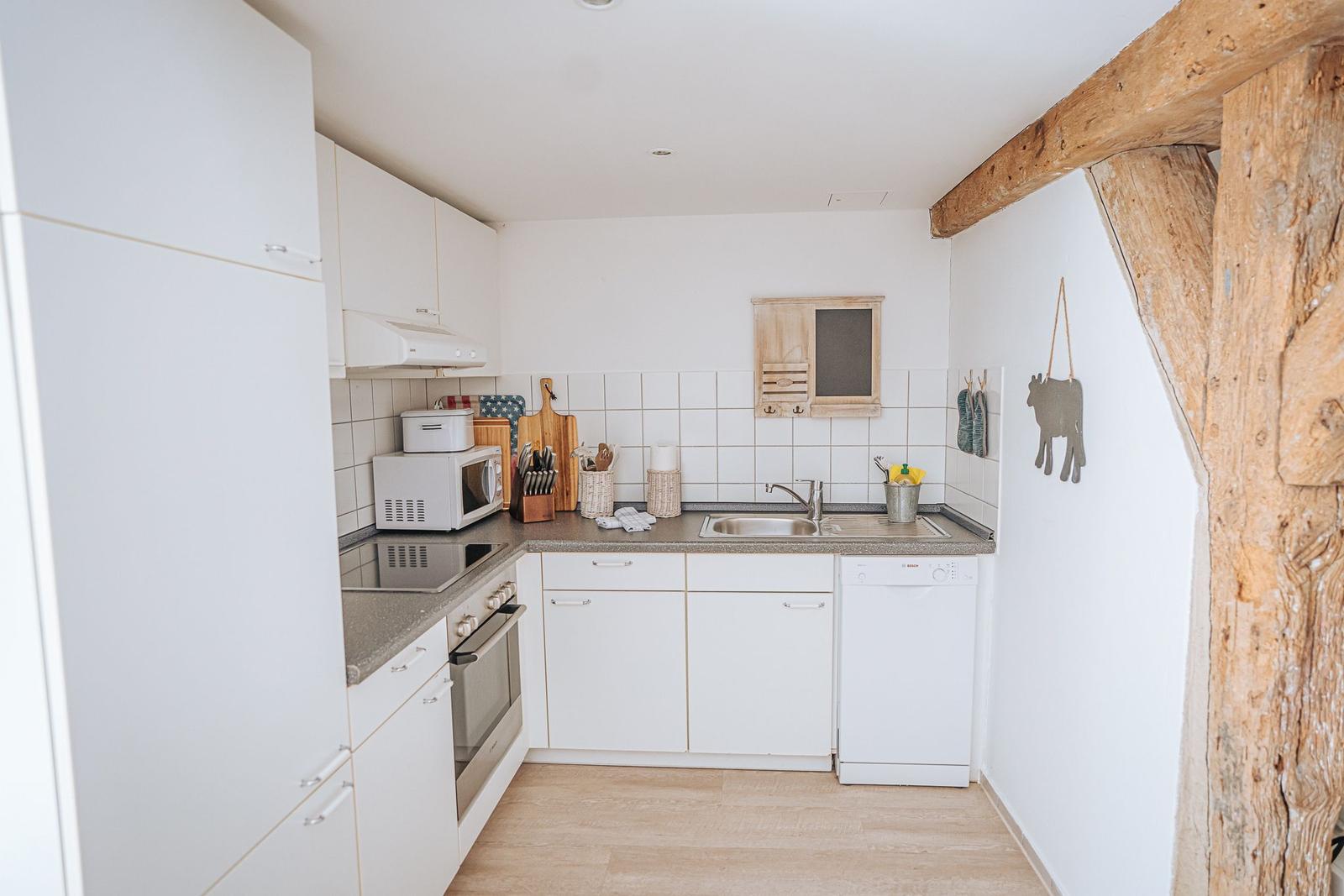 Küche mit weißen Schränken, Spüle und Waschmaschine. Holzbalken an der Wand.