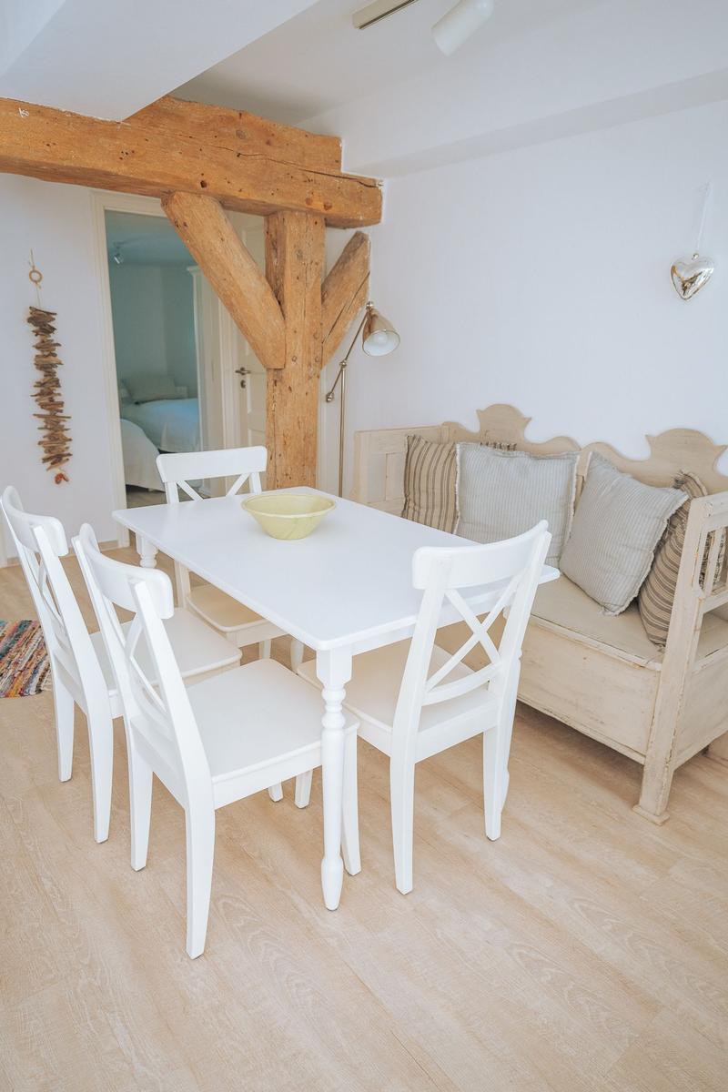 Essbereich mit weißem Tisch und Stühlen, Holzbank und Balken.