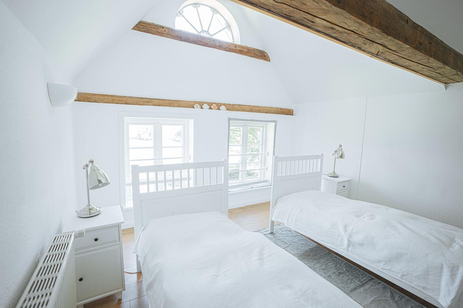 Zwei Betten mit weißen Laken, zwei Nachttische und Fenster mit Blick nach draußen.