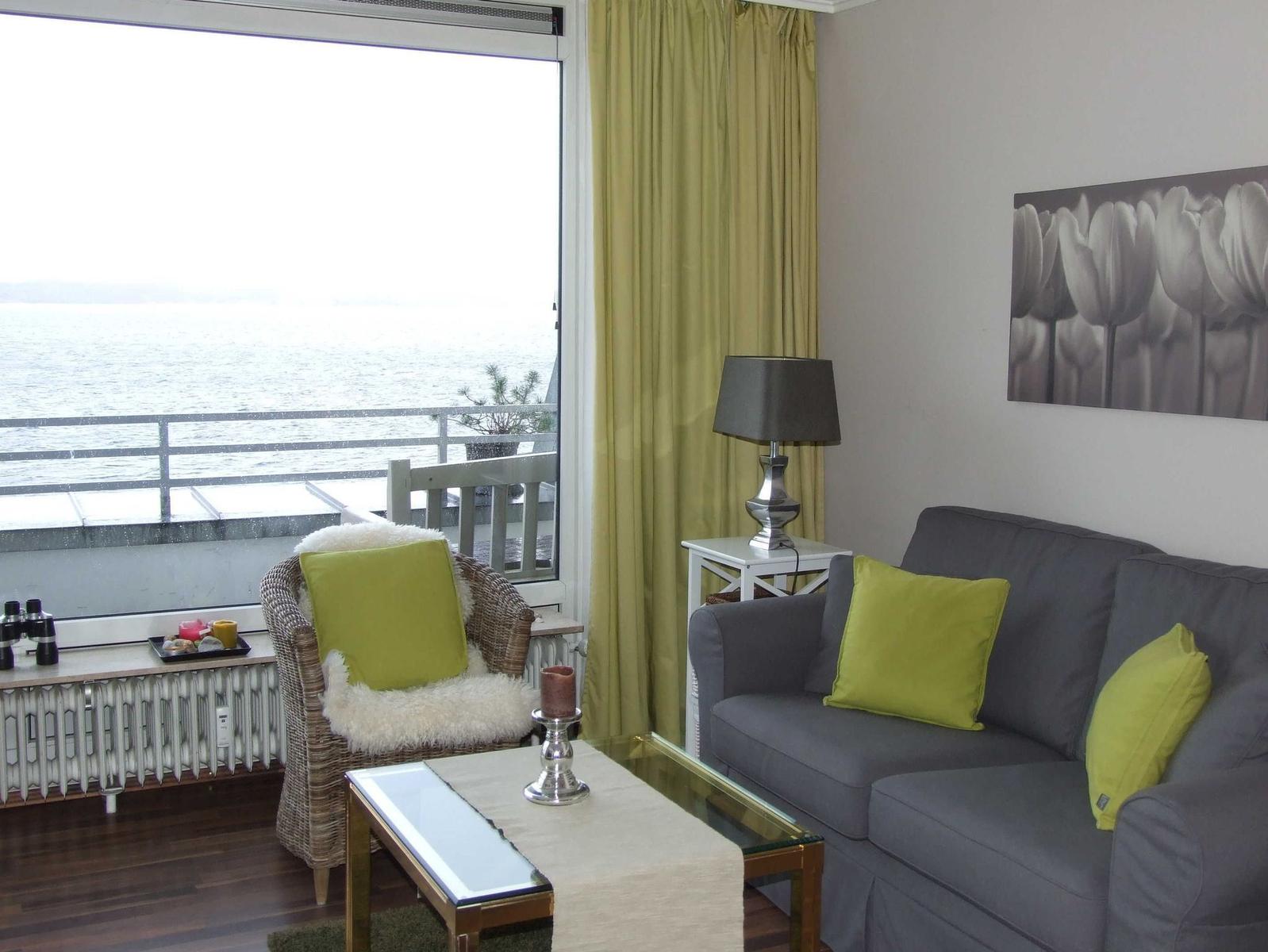 Wohnzimmer mit Sofa, Sessel und Meerblick durch großes Fenster.