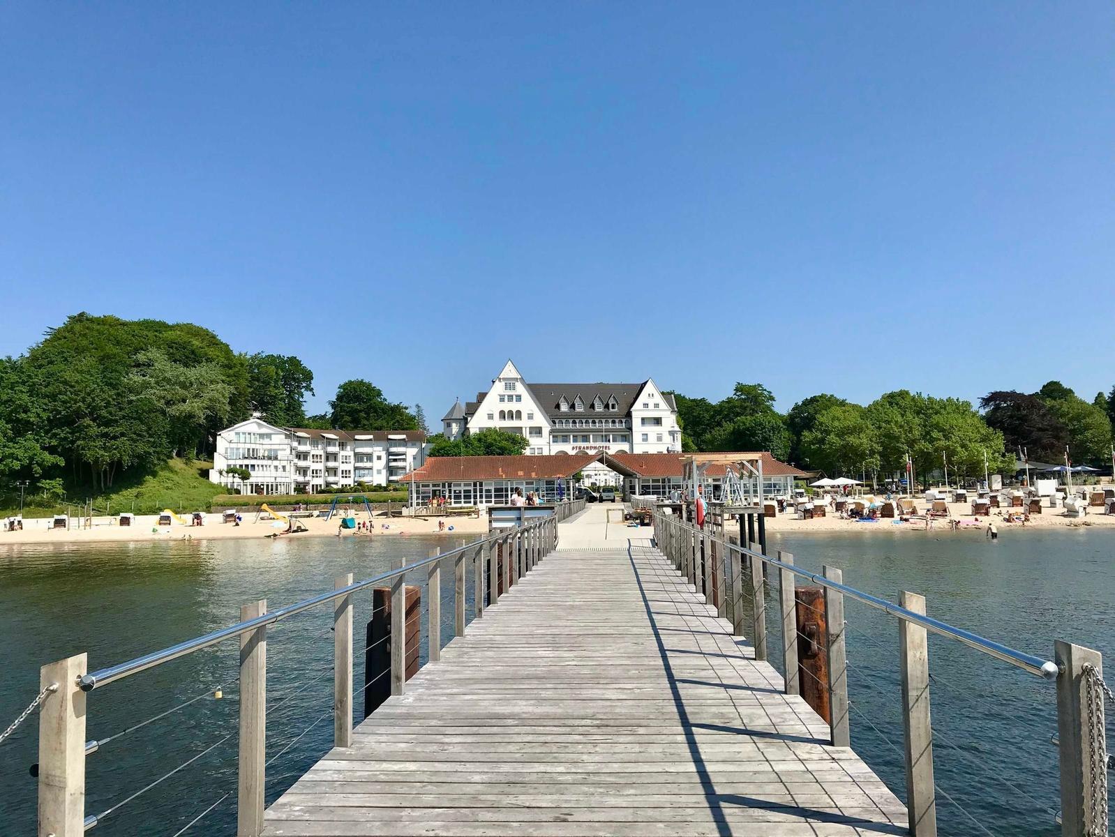Holzbrücke führt zum Strandhotel mit Strand und Badegästen.