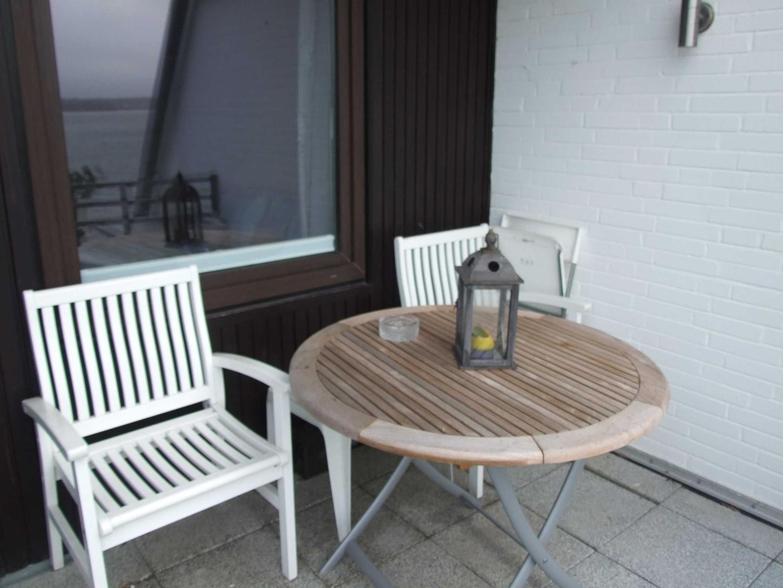 Terrasse mit runden Tisch und zwei weißen Stühlen. Hintergrund: Fenster und weißer Ziegelstein.
