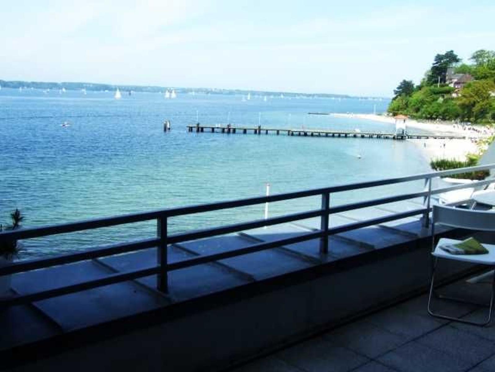 Terrasse mit Blick auf See und Strand. Bootssteg und Segelboote sind sichtbar.