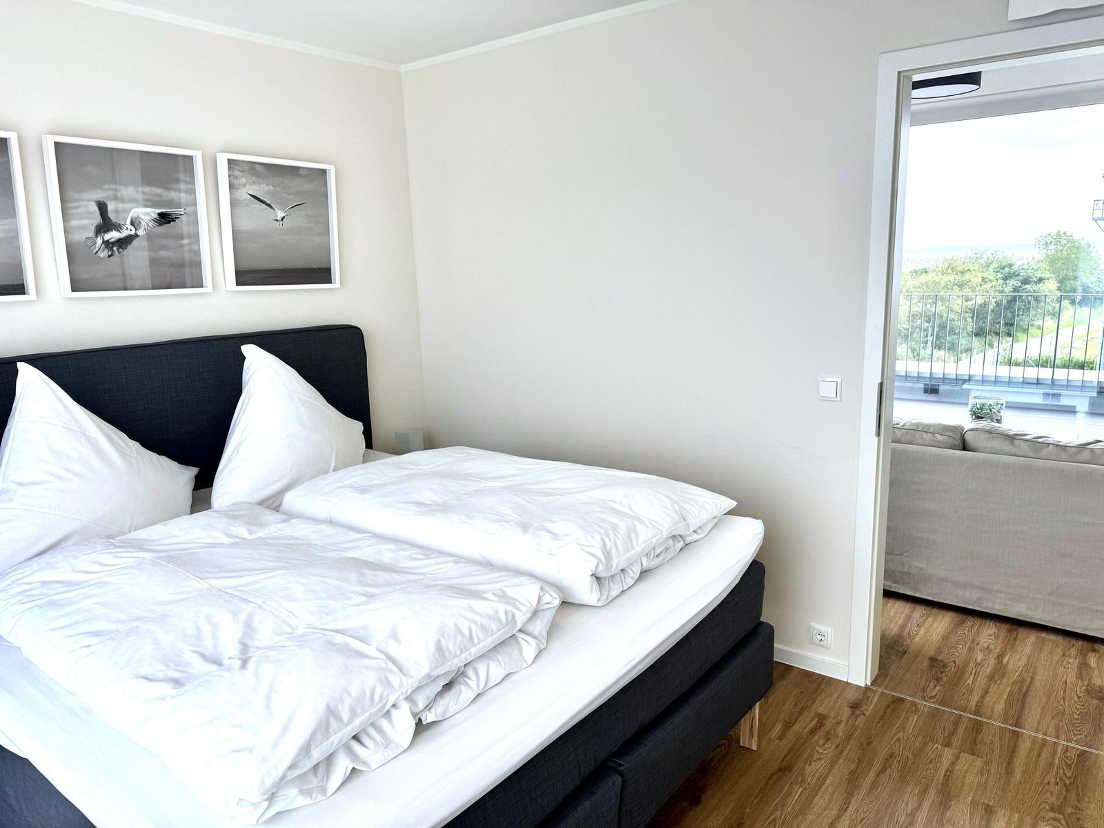 Schlafzimmer mit Doppelbett, Wandbildern und Zugang zum Balkon.