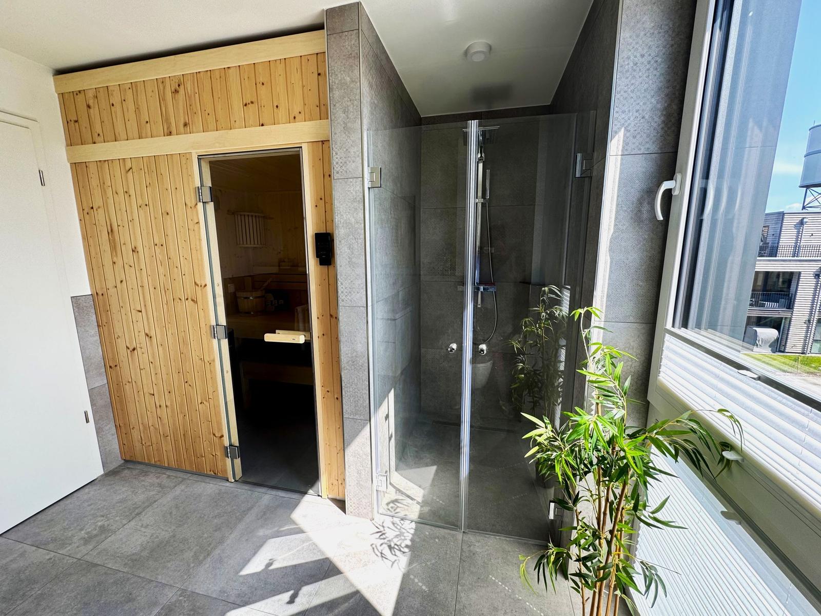 Dusche mit Glaswand und Sauna mit Holztür