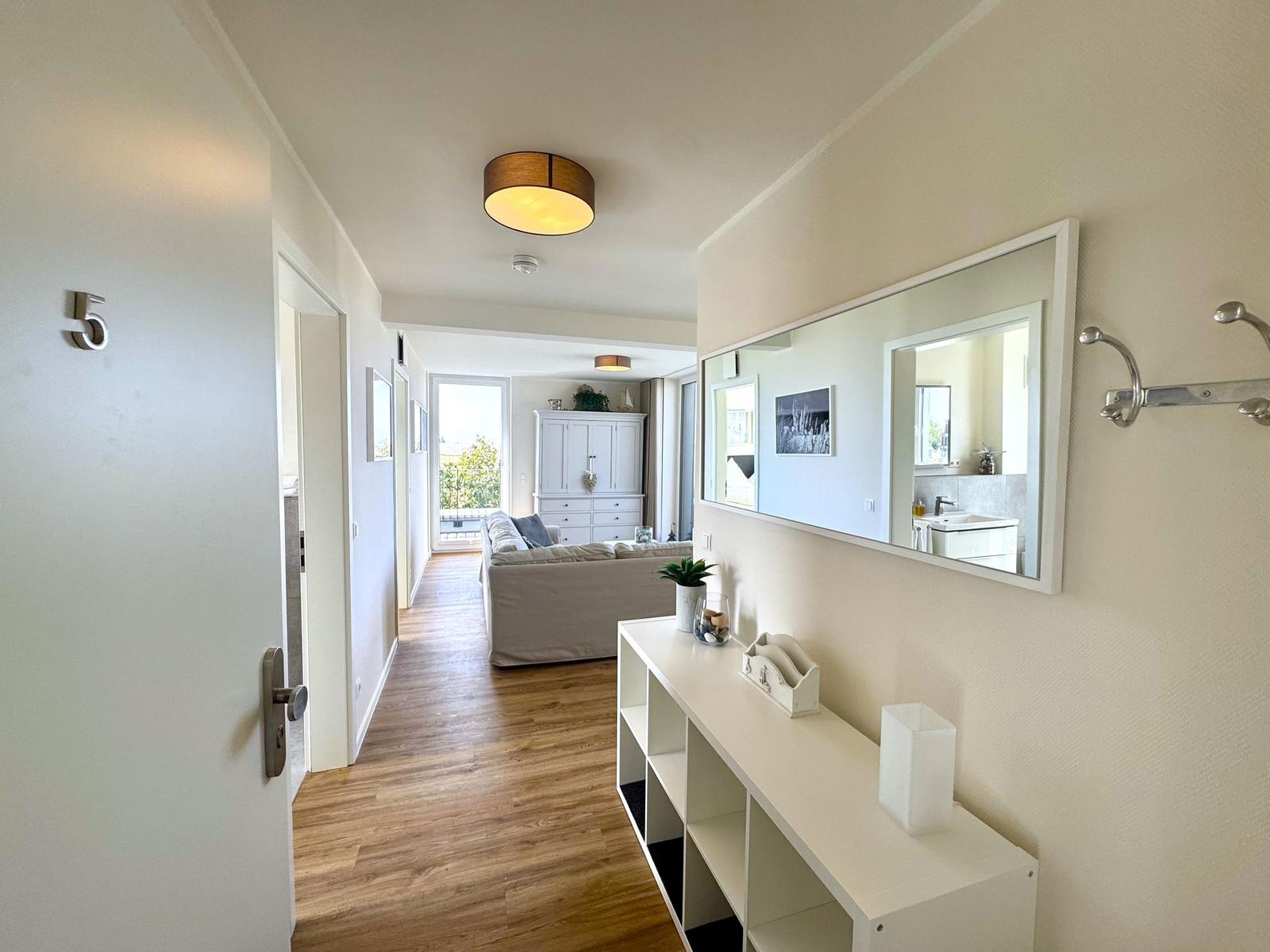 Flur mit Spiegel, Schrank und Blick in Wohnzimmer mit Sofa und Balkon.